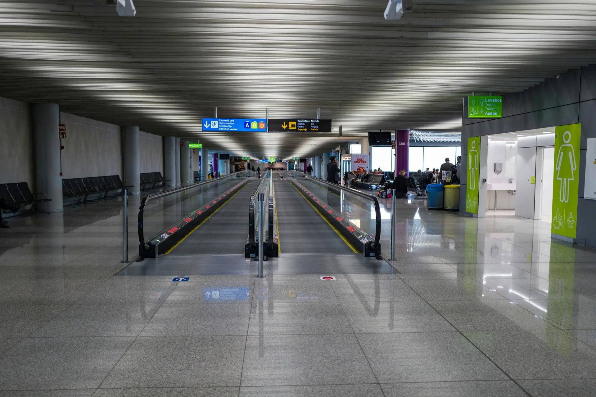 A long, bright airport concourse with moving walkways stretching into the distance.