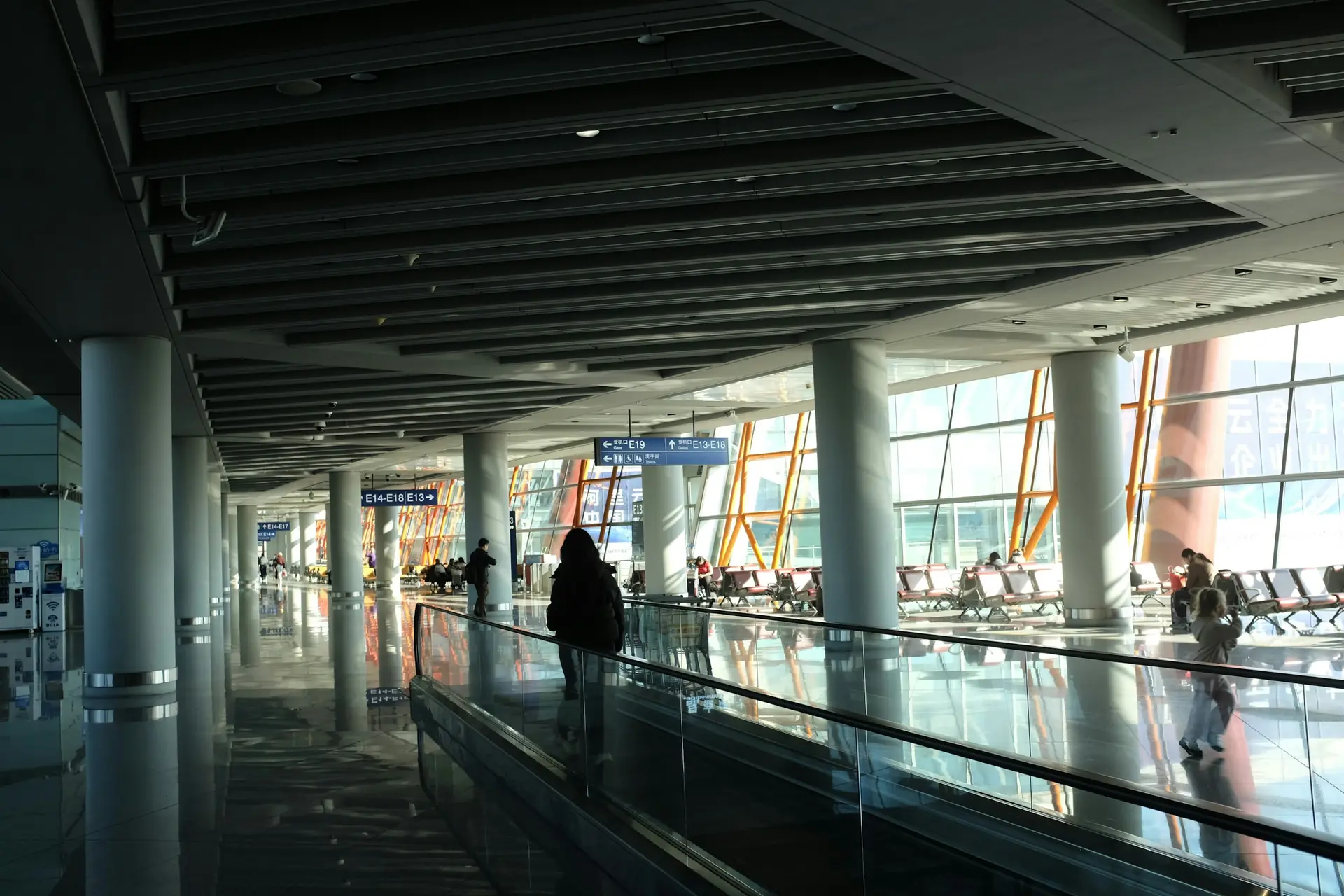 A traveler on a moving walkway in a warmly lit airport terminal.